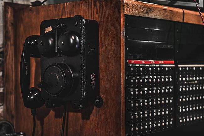 Een zwarte telefoon hangt aan een houten muur naast een houten doos.