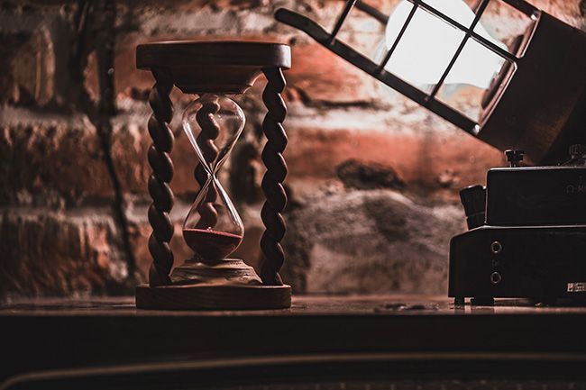 Een houten zandloper staat op een houten tafel.