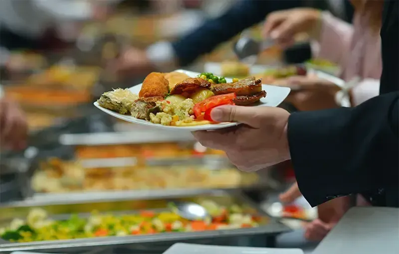Een persoon houdt een bord met eten vast bij een buffet.