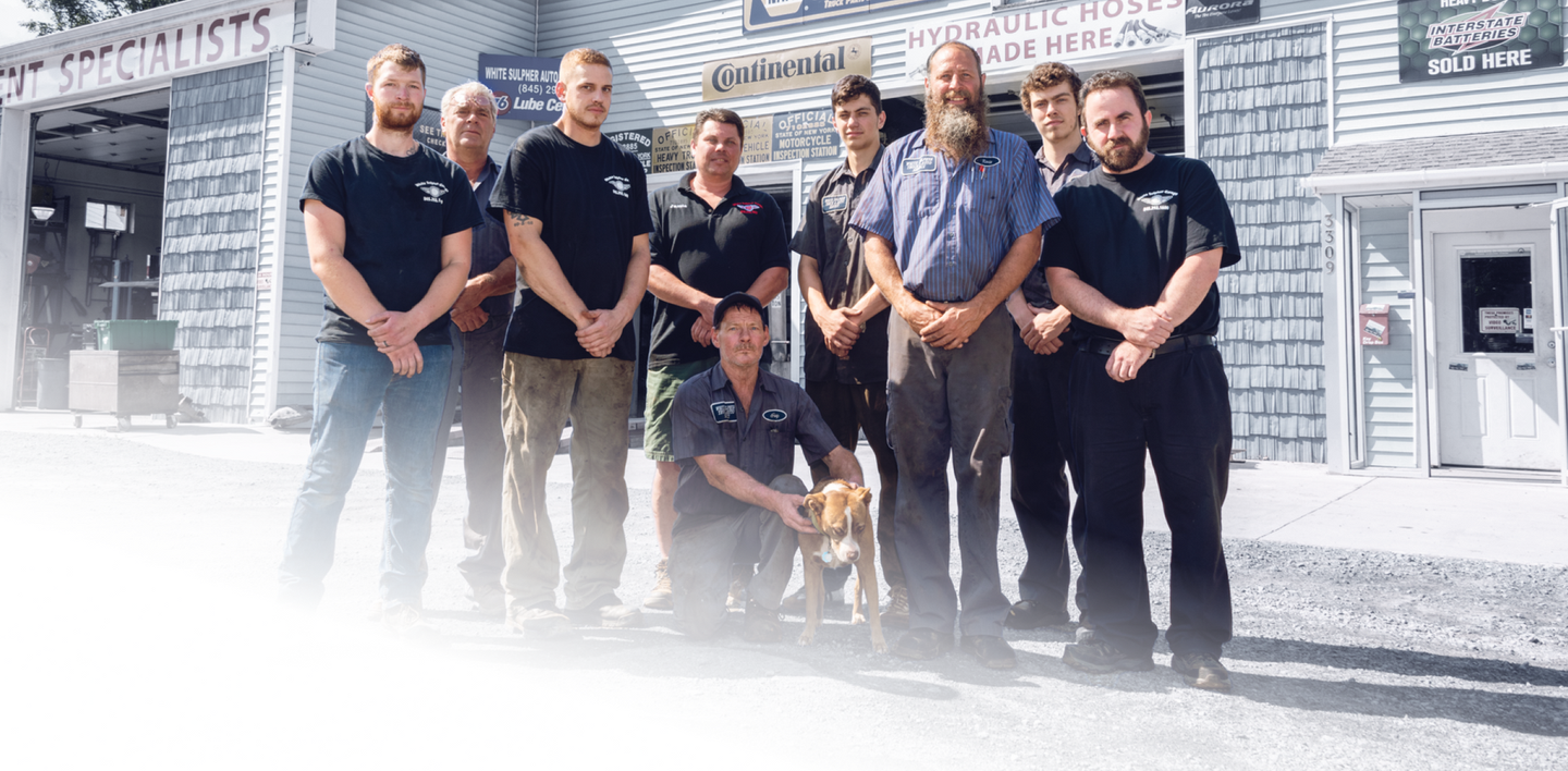 A group of men are posing for a picture in front of a building. | White Sulphur Garage