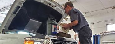 A man is working on a truck in a garage with the hood open. | White Sulphur Garage