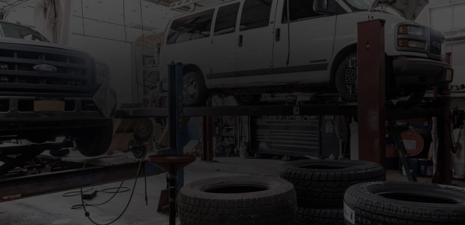 A van is sitting on a lift in a garage next to a pile of tires. | White Sulphur Garage