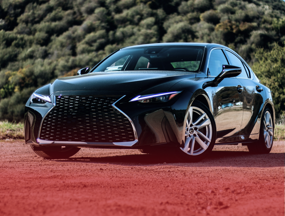 A black lexus is parked on a dirt road in front of a forest. | White Sulphur Garage