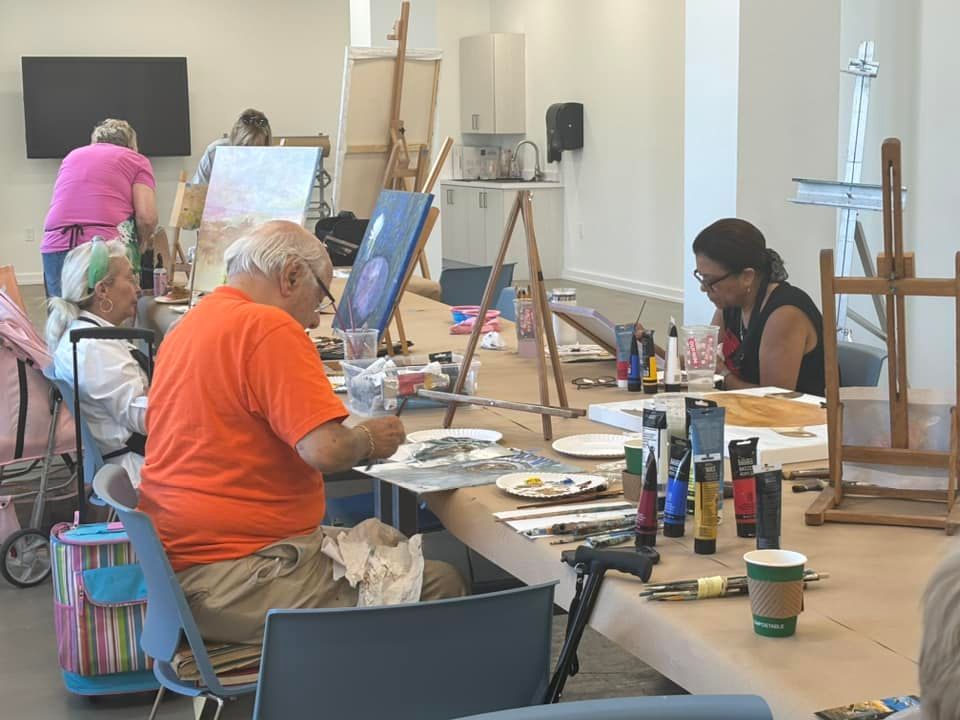 A group of people are sitting at a table painting