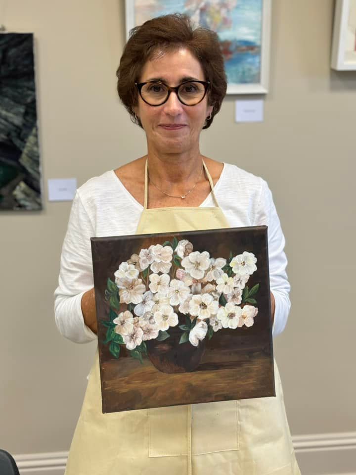 A woman is holding a painting of white flowers in a vase.