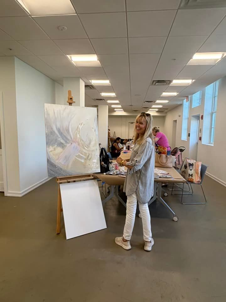 A woman is painting a picture on an easel in a large room.