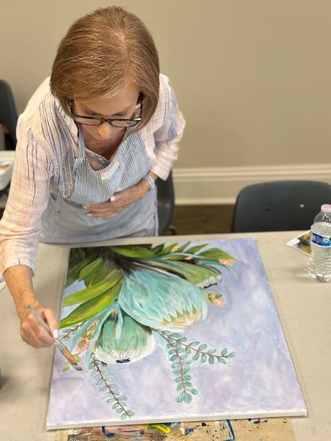 A woman is painting a picture of a flower on a canvas.