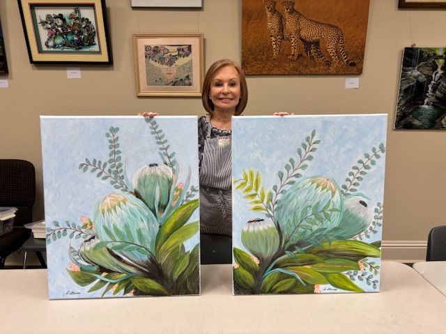 A woman is holding two paintings of flowers on a table