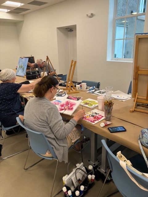 A group of people are sitting at a table painting.