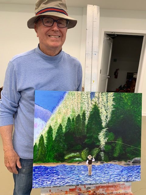 A man in a hat is holding a painting of a man fishing in a river