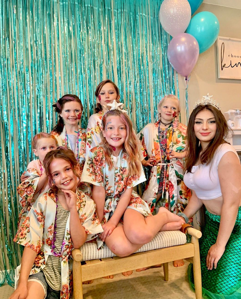 A group of children are posing for a picture with a woman dressed as a mermaid.