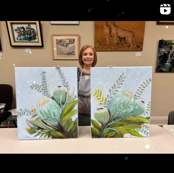 A woman is holding two paintings of flowers on a table