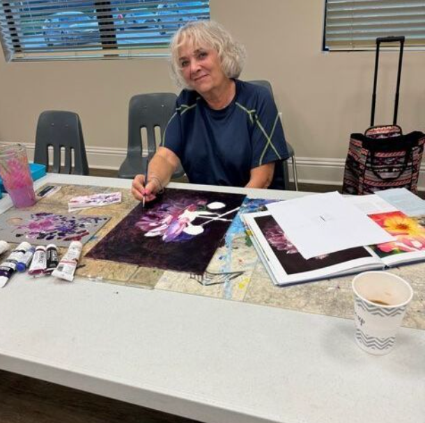 A woman is sitting at a table painting a picture