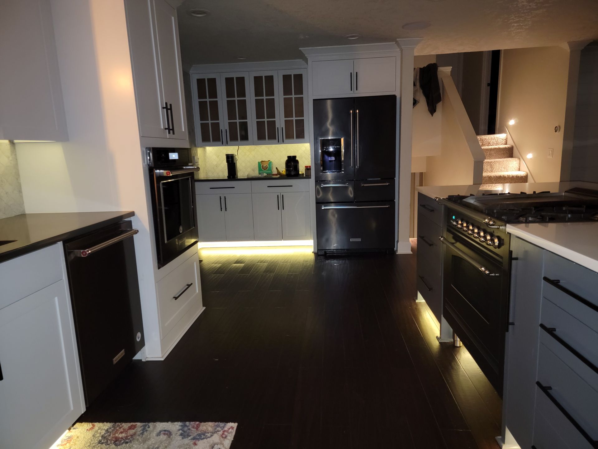 Kitchen with dark wood floors, white and gray cabinets, stainless steel appliances, and under-cabinet lighting.