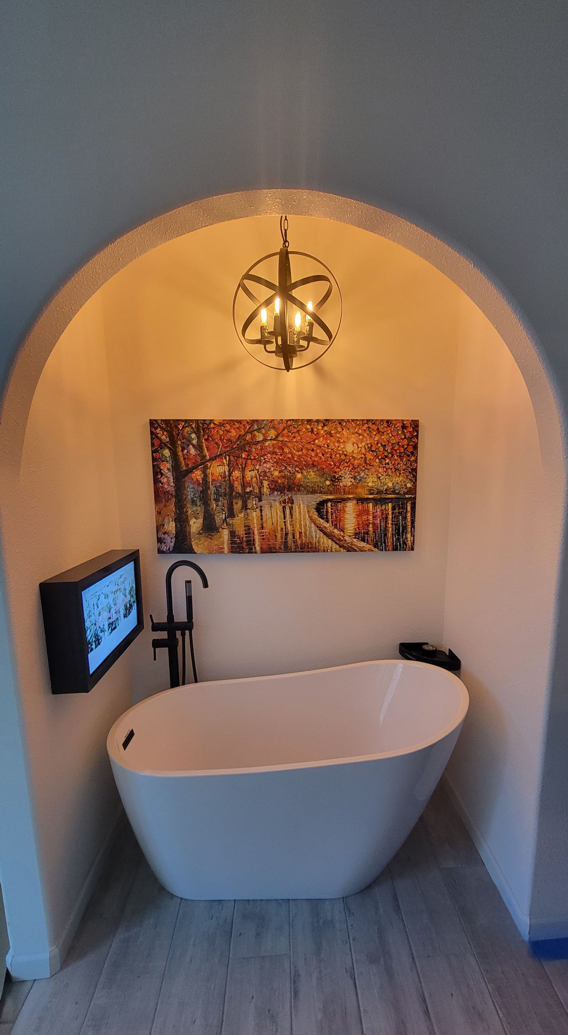 Bathroom niche with a freestanding white tub, art, a TV, and a pendant light.