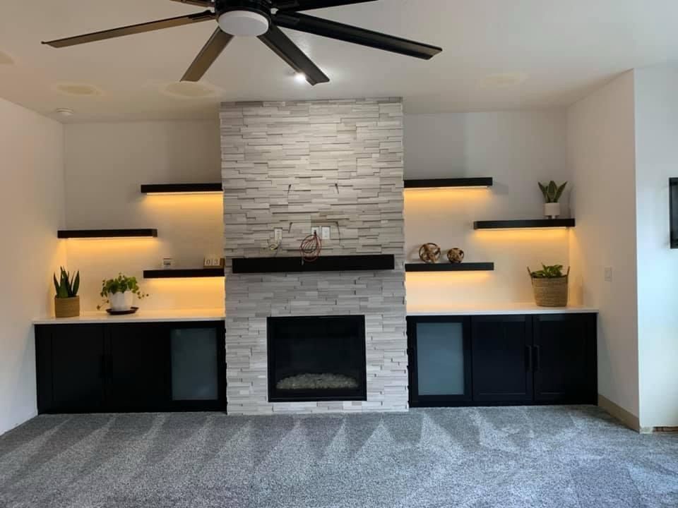 Modern fireplace with stone surround, floating shelves with plants, black cabinets, and recessed lighting.