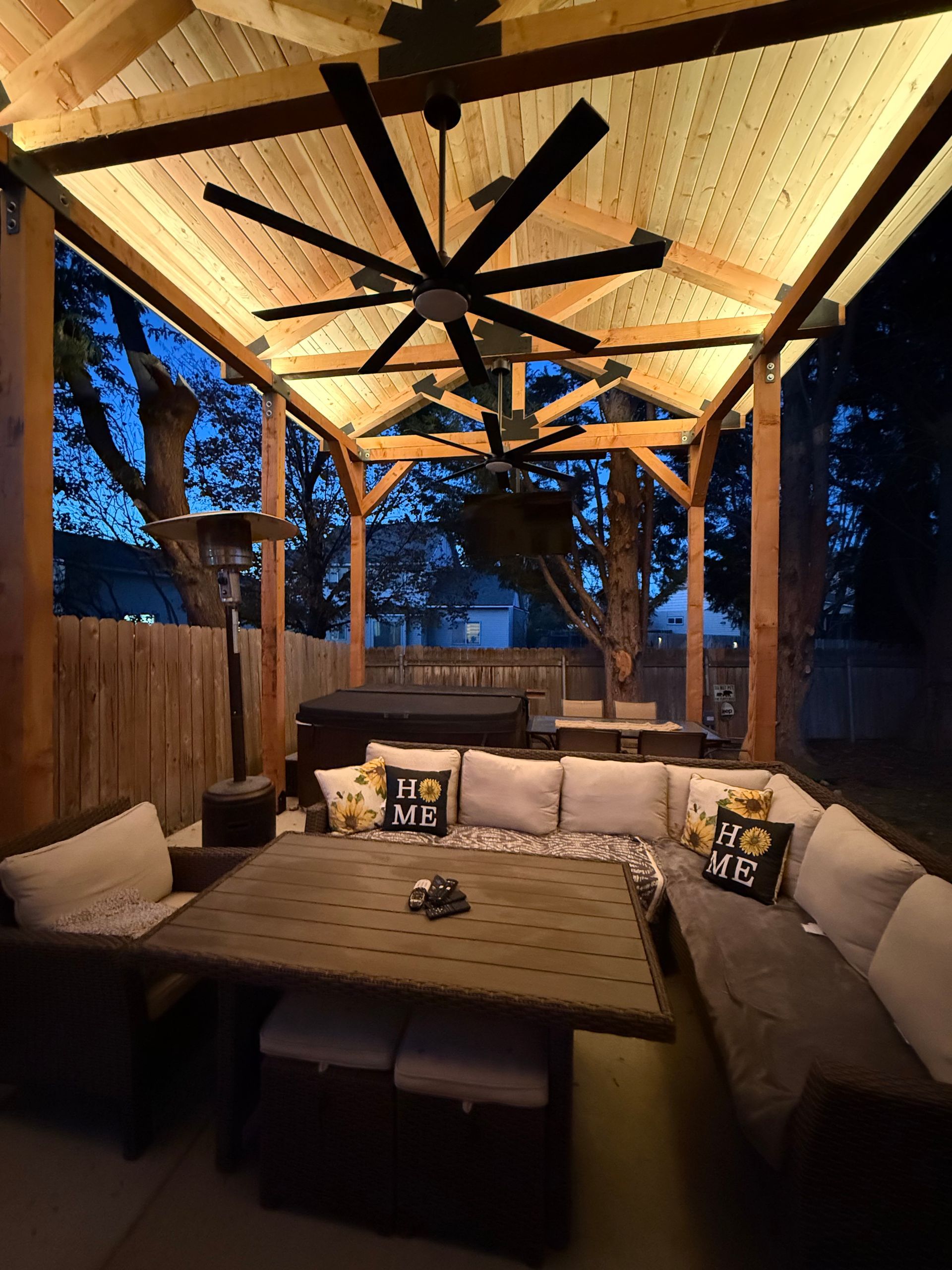 Outdoor gazebo with seating, a large ceiling fan, and built-in lighting at night.