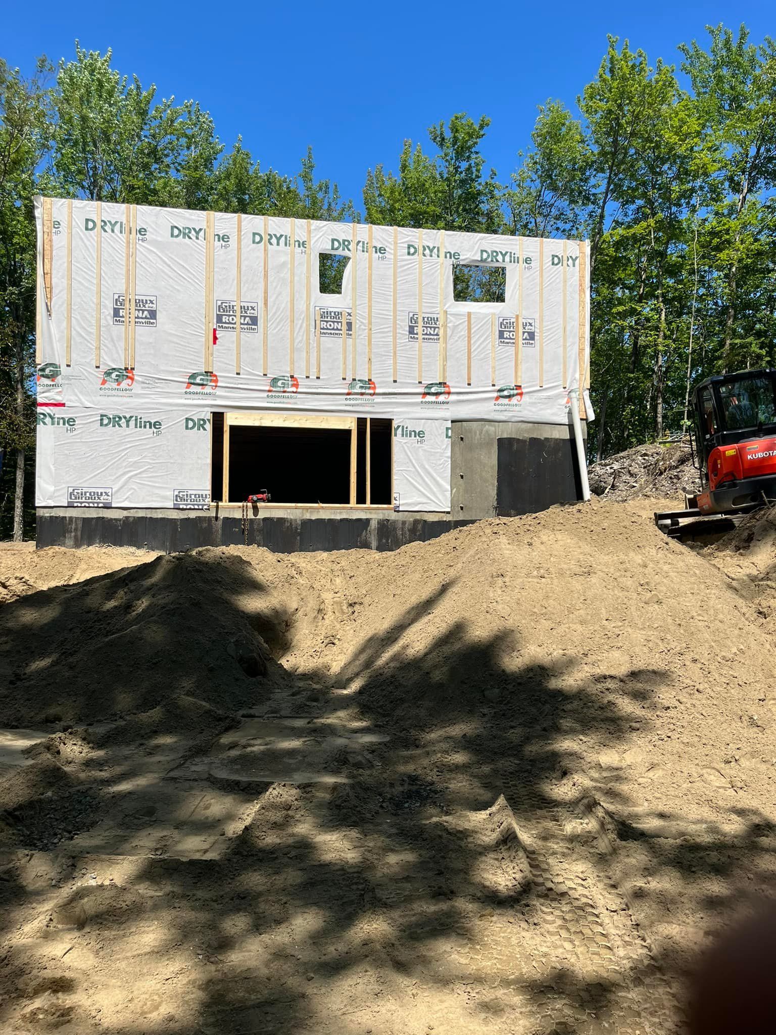 Chantier : Bâtiment inachevé avec des panneaux de contreplaqué, des fenêtres et de la terre autour.