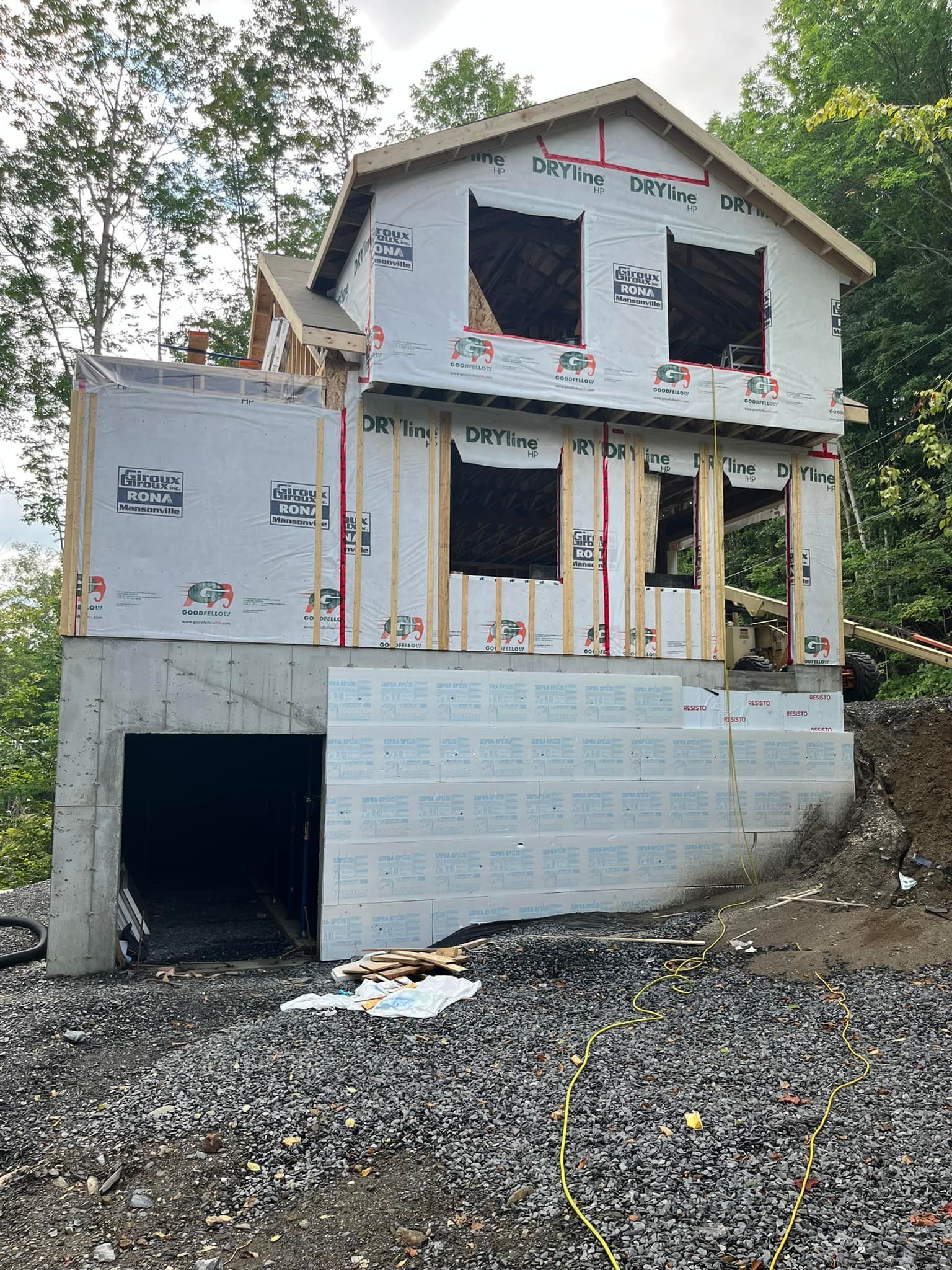 Maison à deux étages en construction. Murs extérieurs recouverts, charpente apparente. Garage au rez-de-chaussée.