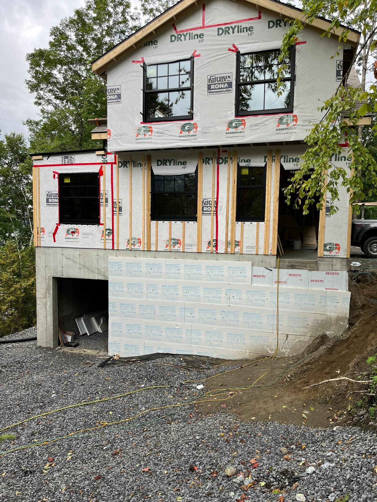 Une maison à deux étages en construction, avec une base en béton et des encadrements de fenêtres noirs.