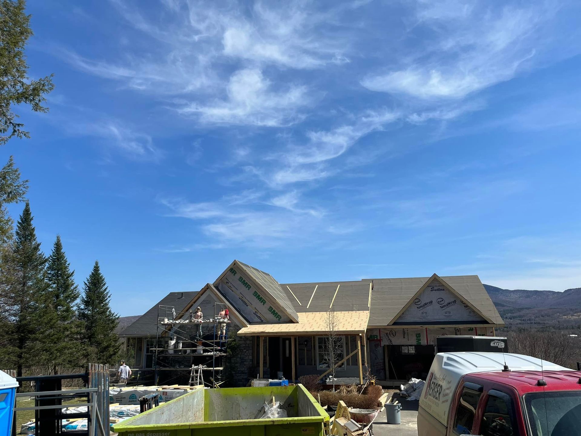 Maison en construction, échafaudages visibles, ciel bleu.