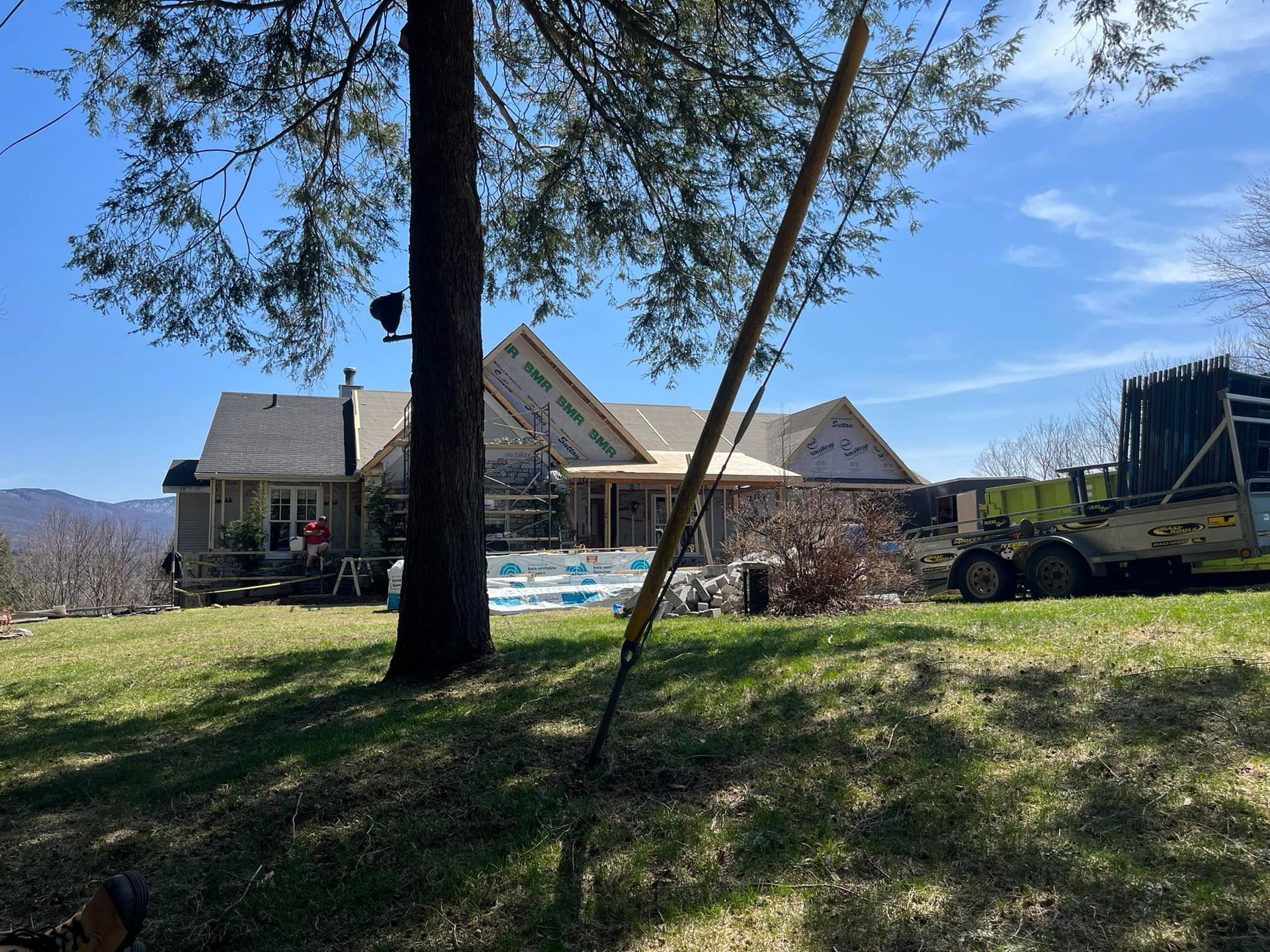 Maison en construction, ouvriers présents, échafaudages et matériaux visibles à l'extérieur par une journée ensoleillée.