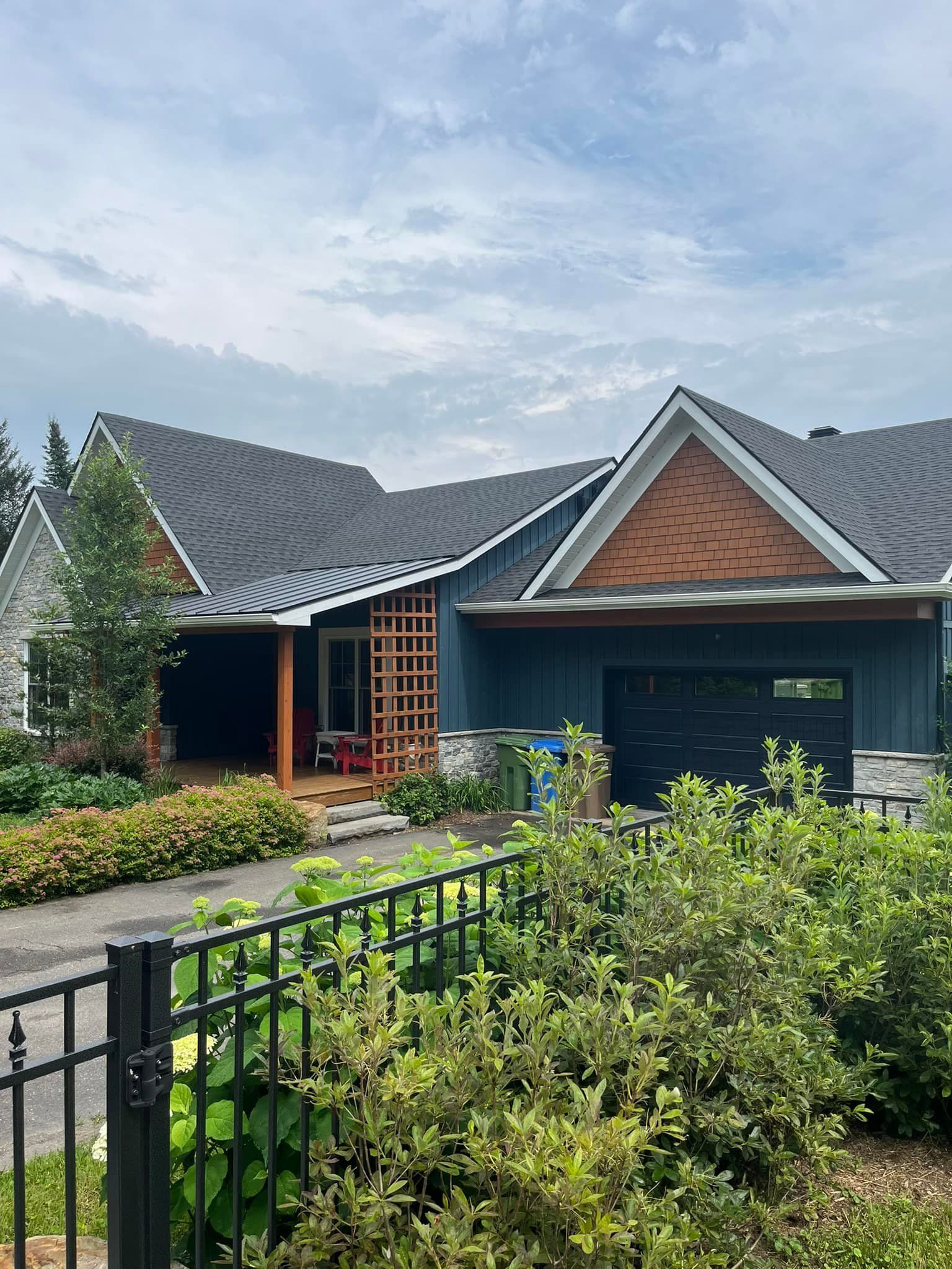 Maison à façade bleue, toit foncé et détails en briques, devant un jardin verdoyant et une clôture noire.