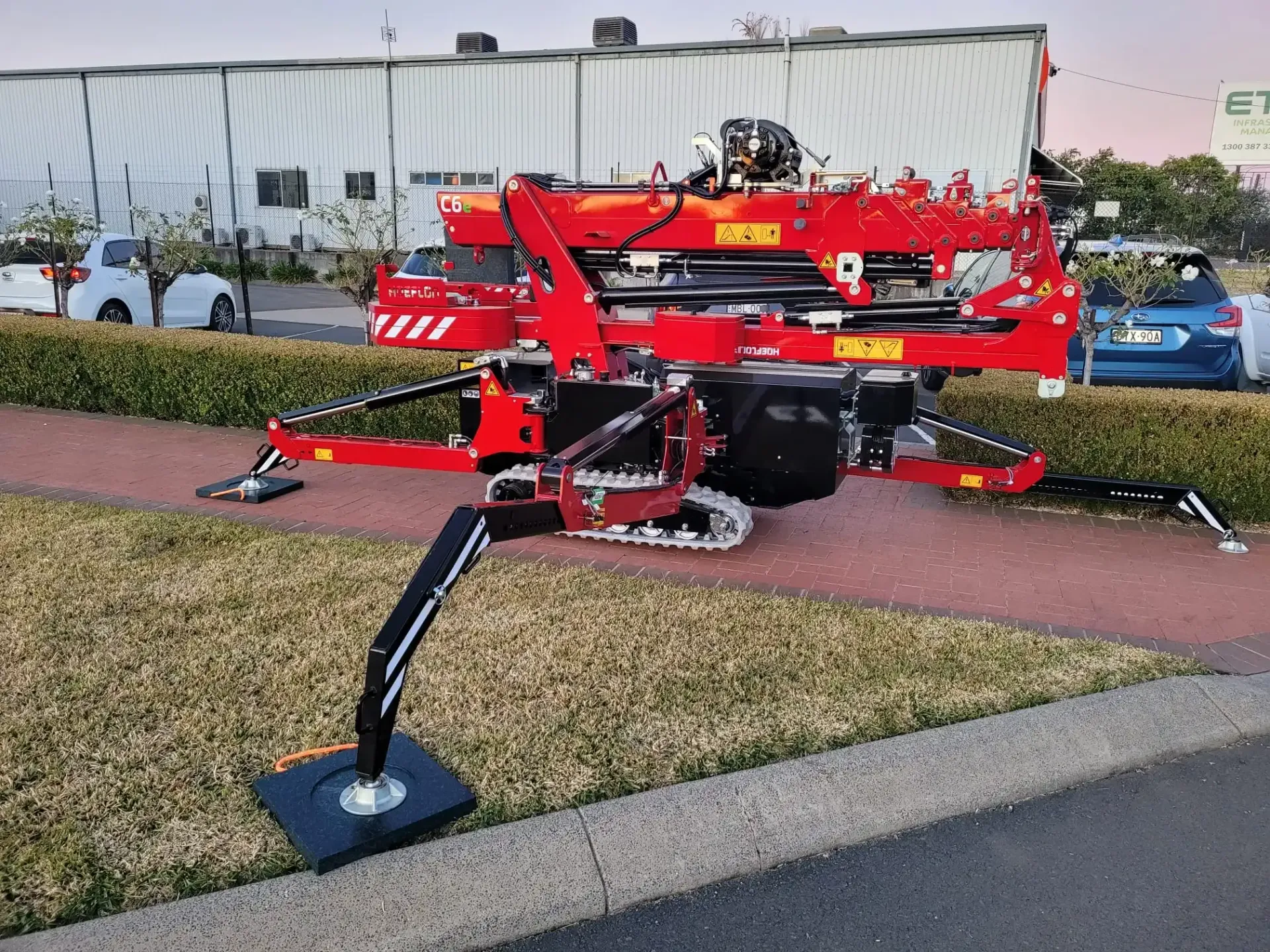 Red spider-like crane on a sidewalk next to a building and cars.