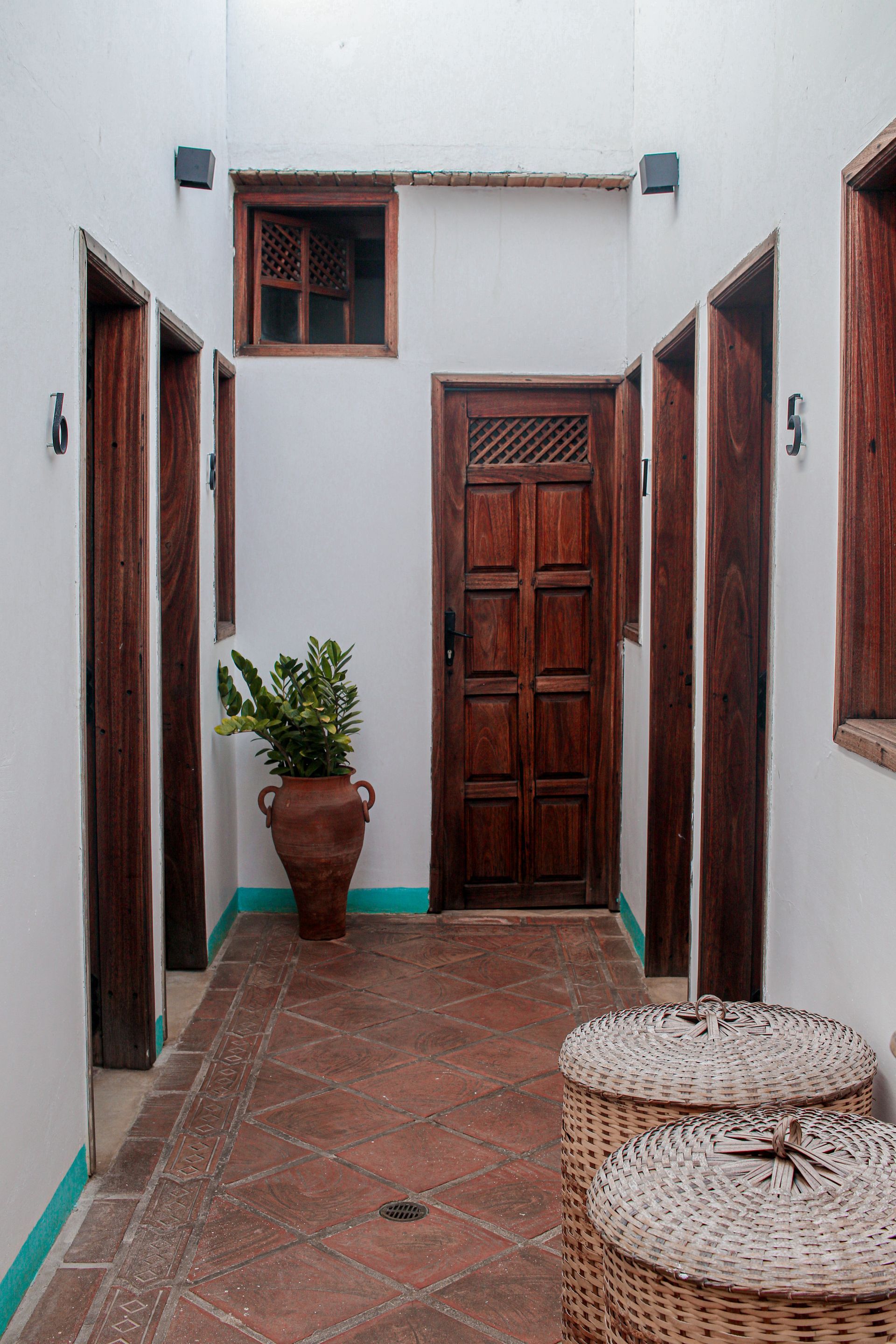 A hallway with a wooden door , wicker baskets and a potted plant.