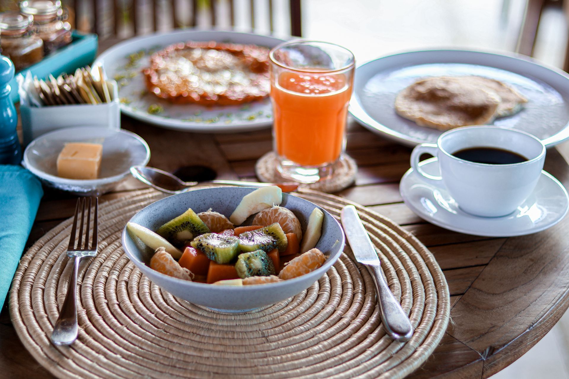 A table topped with plates of food , a bowl of fruit , a cup of coffee and a glass of orange juice.