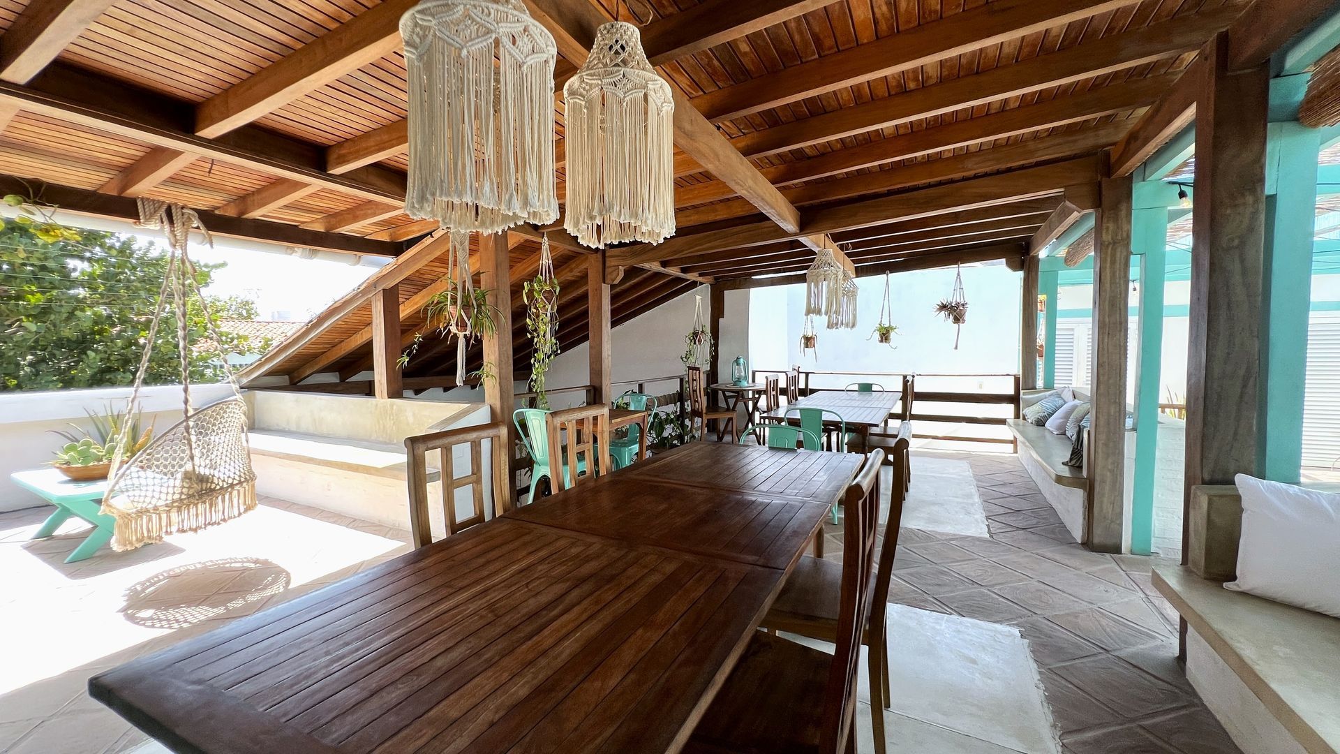 A dining room with a long wooden table and chairs under a wooden roof.