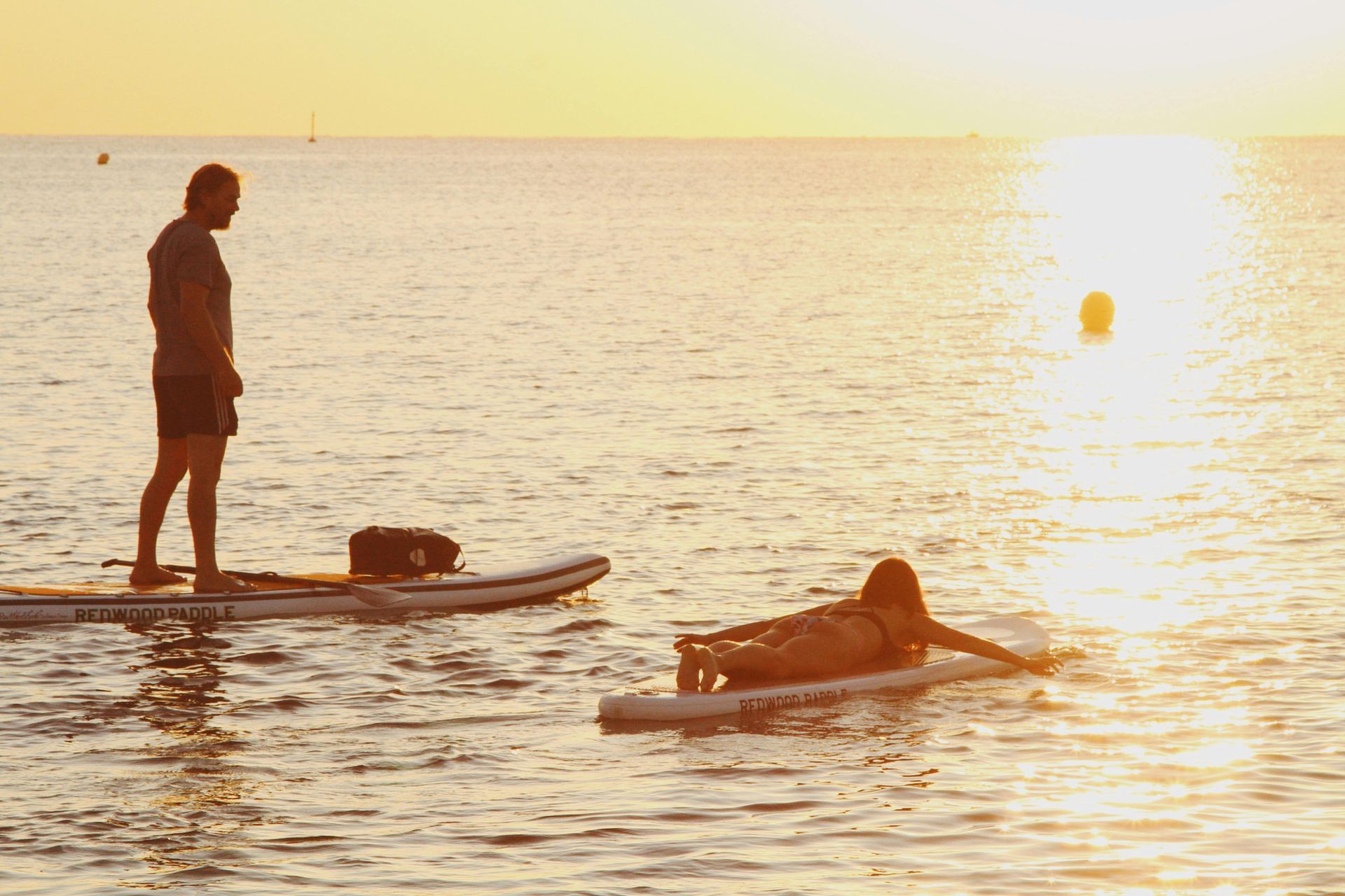 A man and a woman are standing on paddle boards in the ocean.