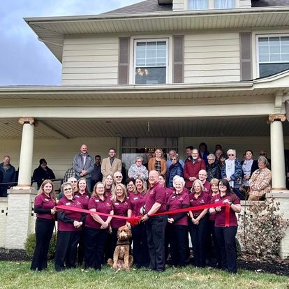 a group of people are standing in front of a house holding a red ribbon Day & Genda Funeral Home Frankfort location.