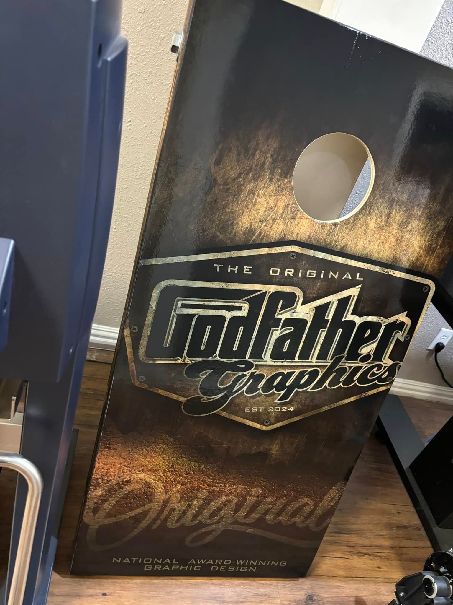 Godfather Graphics cornhole board with gold lettering, hole, and black and gold design.