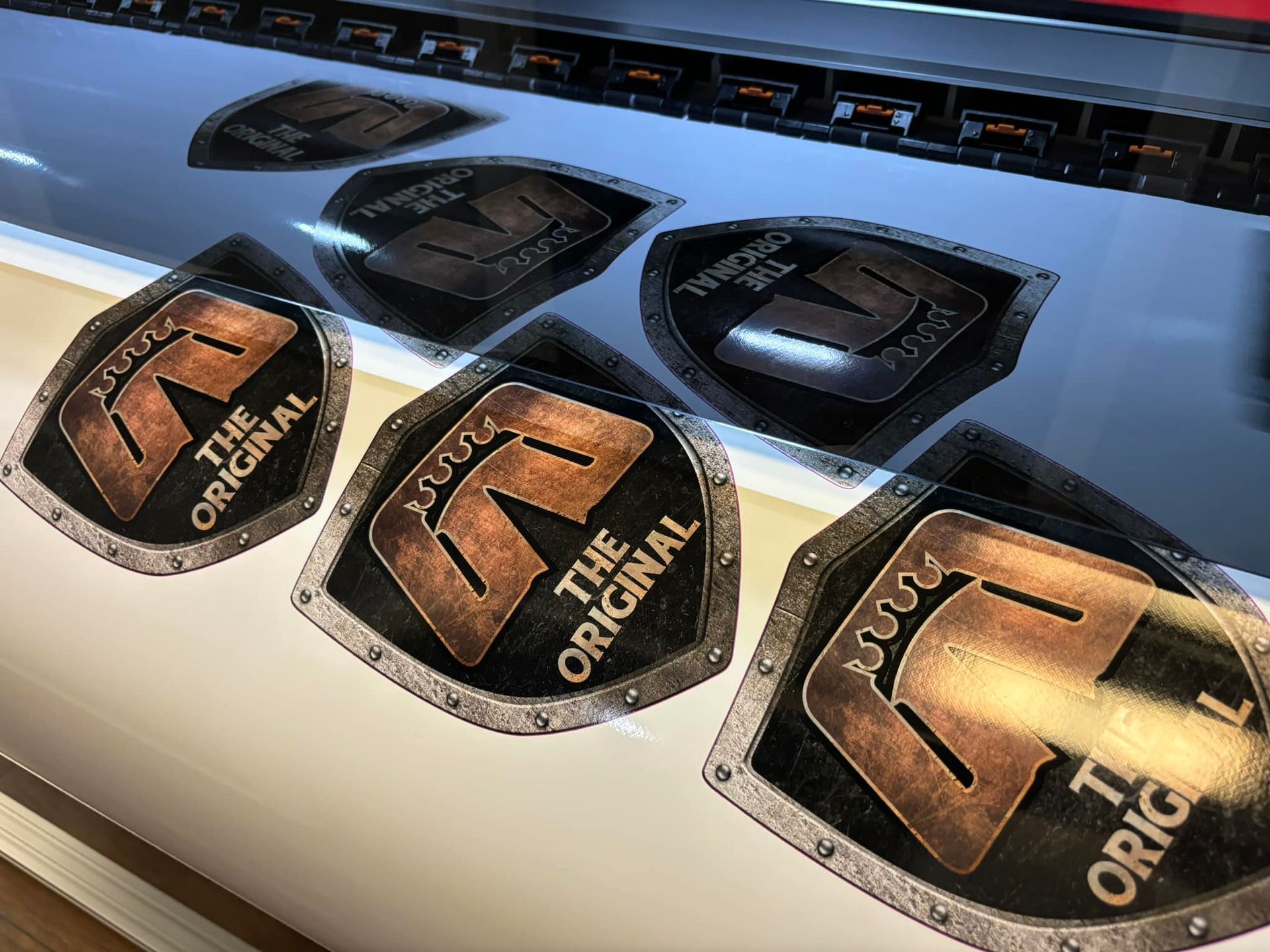 Close-up of printed logos on a wide printer. The logos are in the shape of a shield.