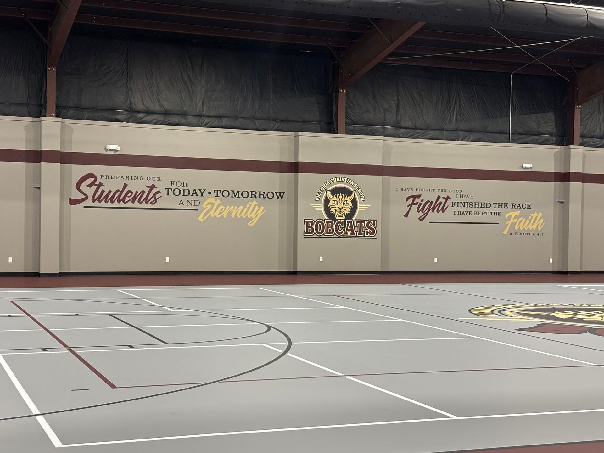 Indoor gymnasium with court lines and motivational wall art featuring school logos and slogans.