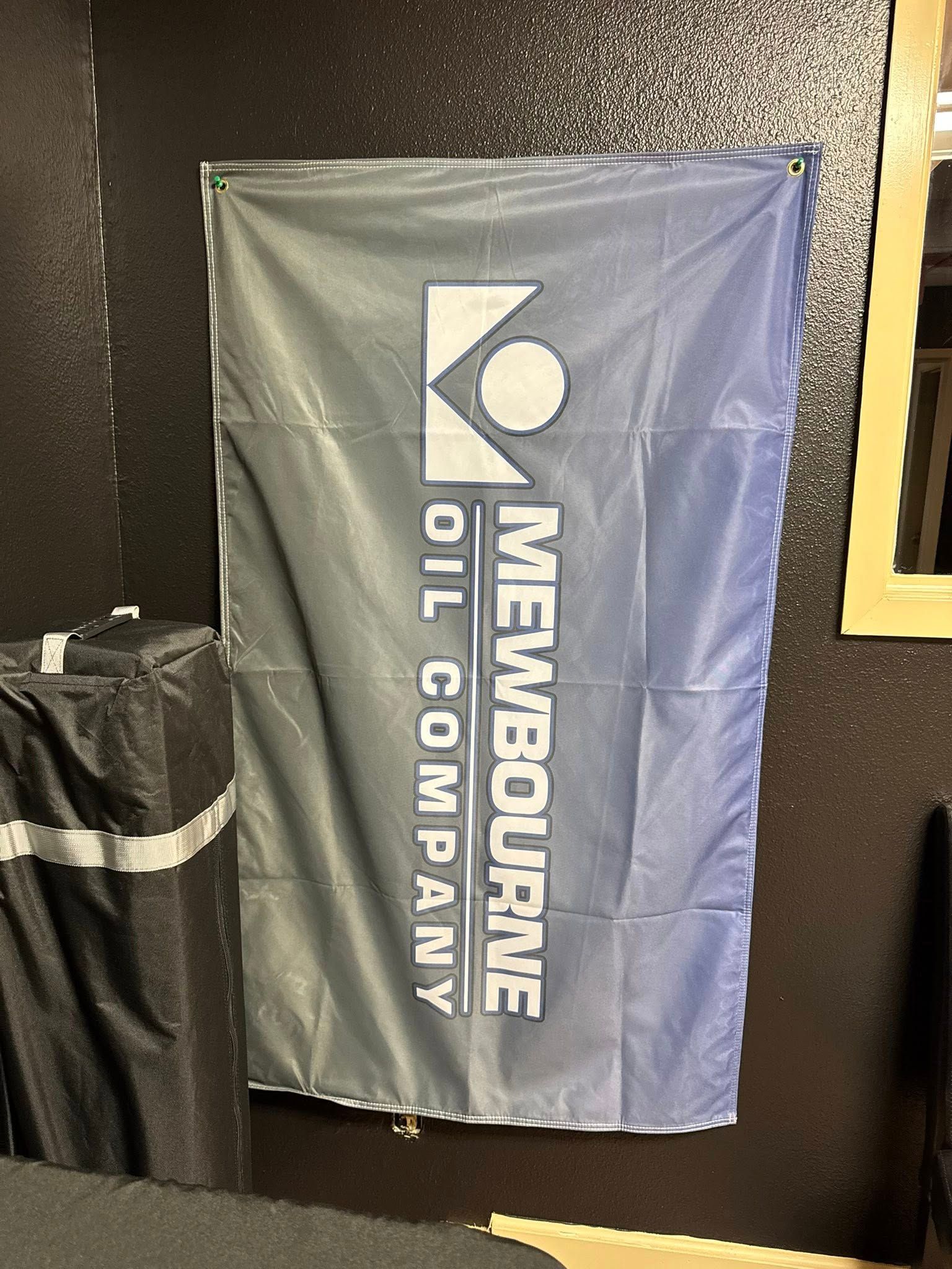 Flag for Mewbourne Oil Company, blue and white logo against a black wall.