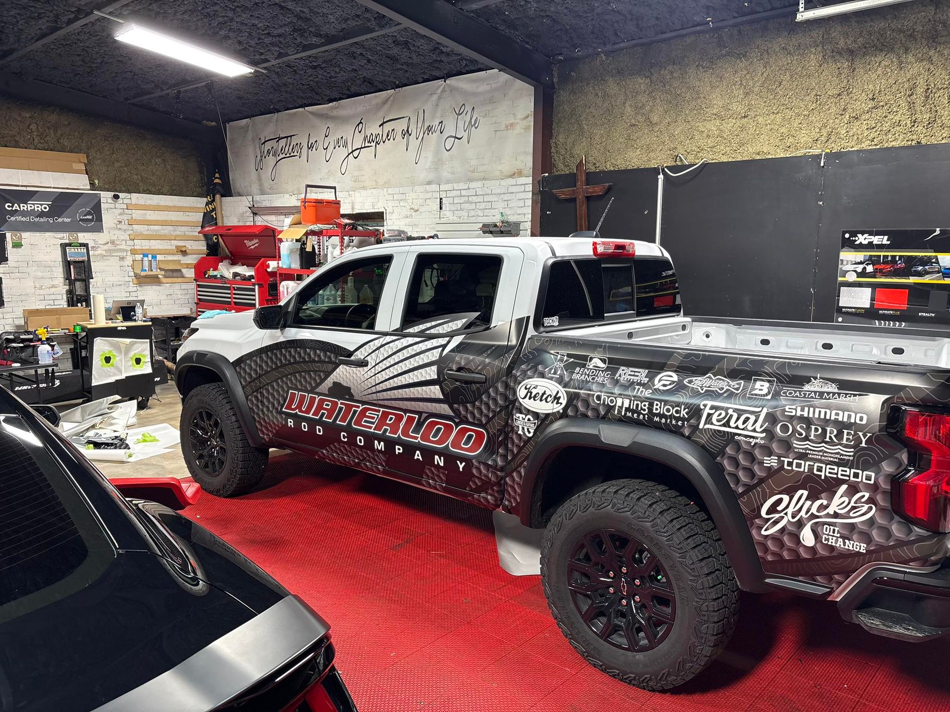 A custom-wrapped Toyota pickup truck inside a garage with a red floor, displaying racing-themed graphics.