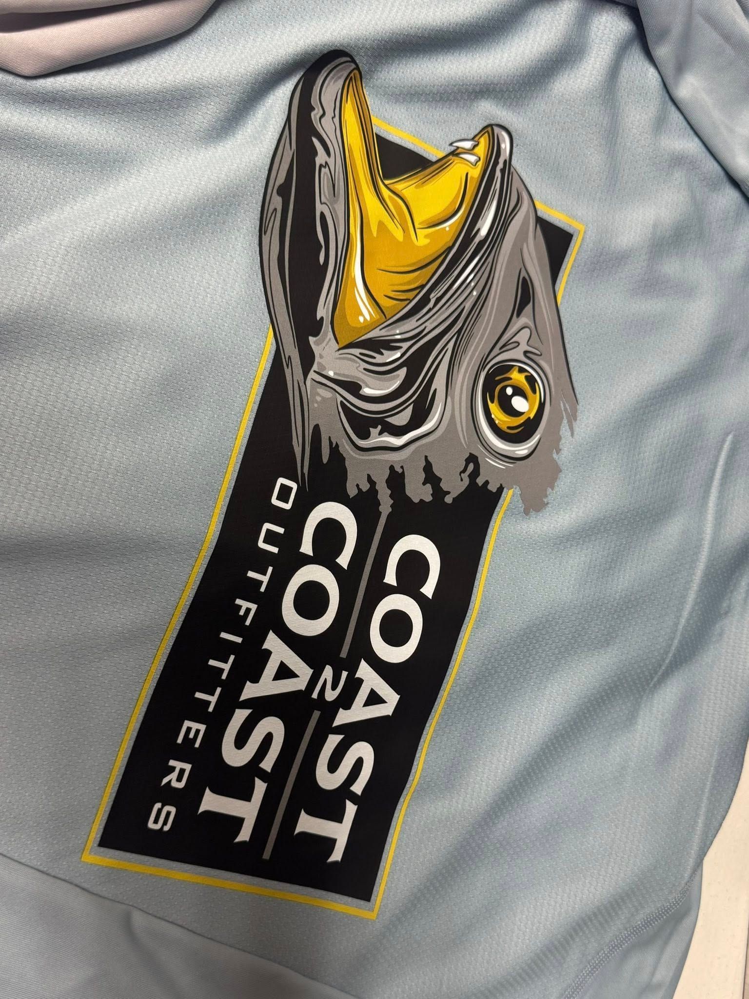 Logo on a light blue shirt: A fish head with an open mouth over a black banner with 