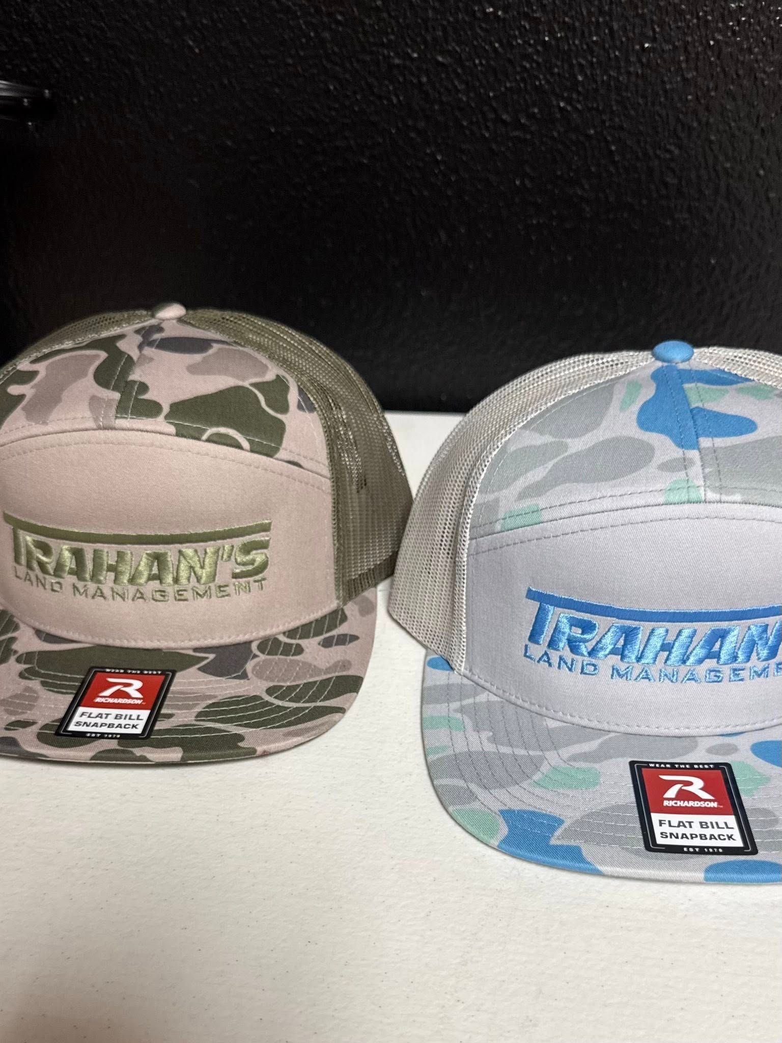 Two camouflage trucker hats side-by-side. One is tan and green, the other is blue and gray. Both have logo patches.