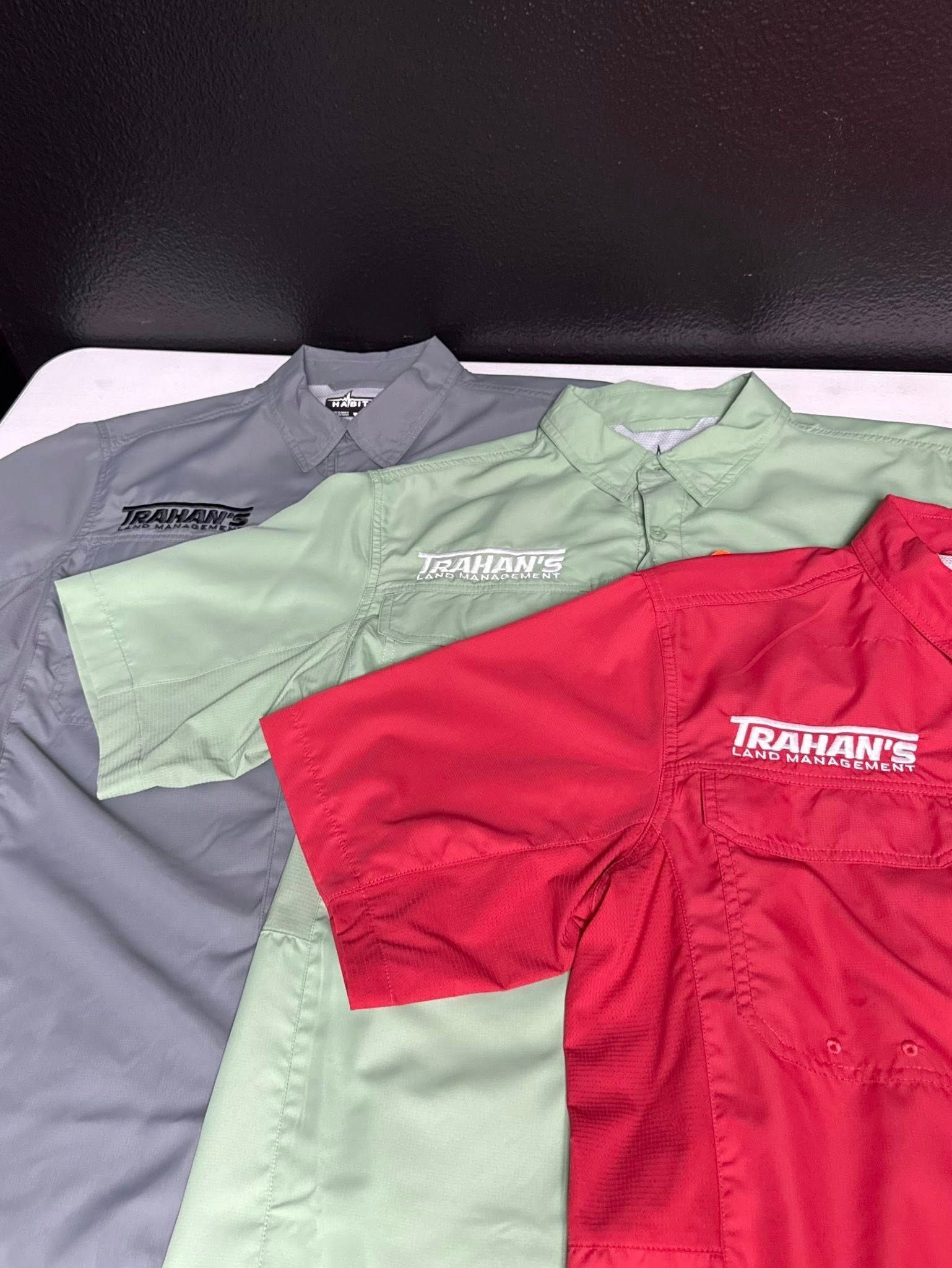 Four short-sleeved shirts in gray, light green, red, and light green, each with a logo on the chest.