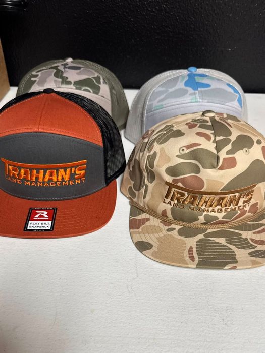 Four baseball caps, each with a different camo pattern or color scheme, with 