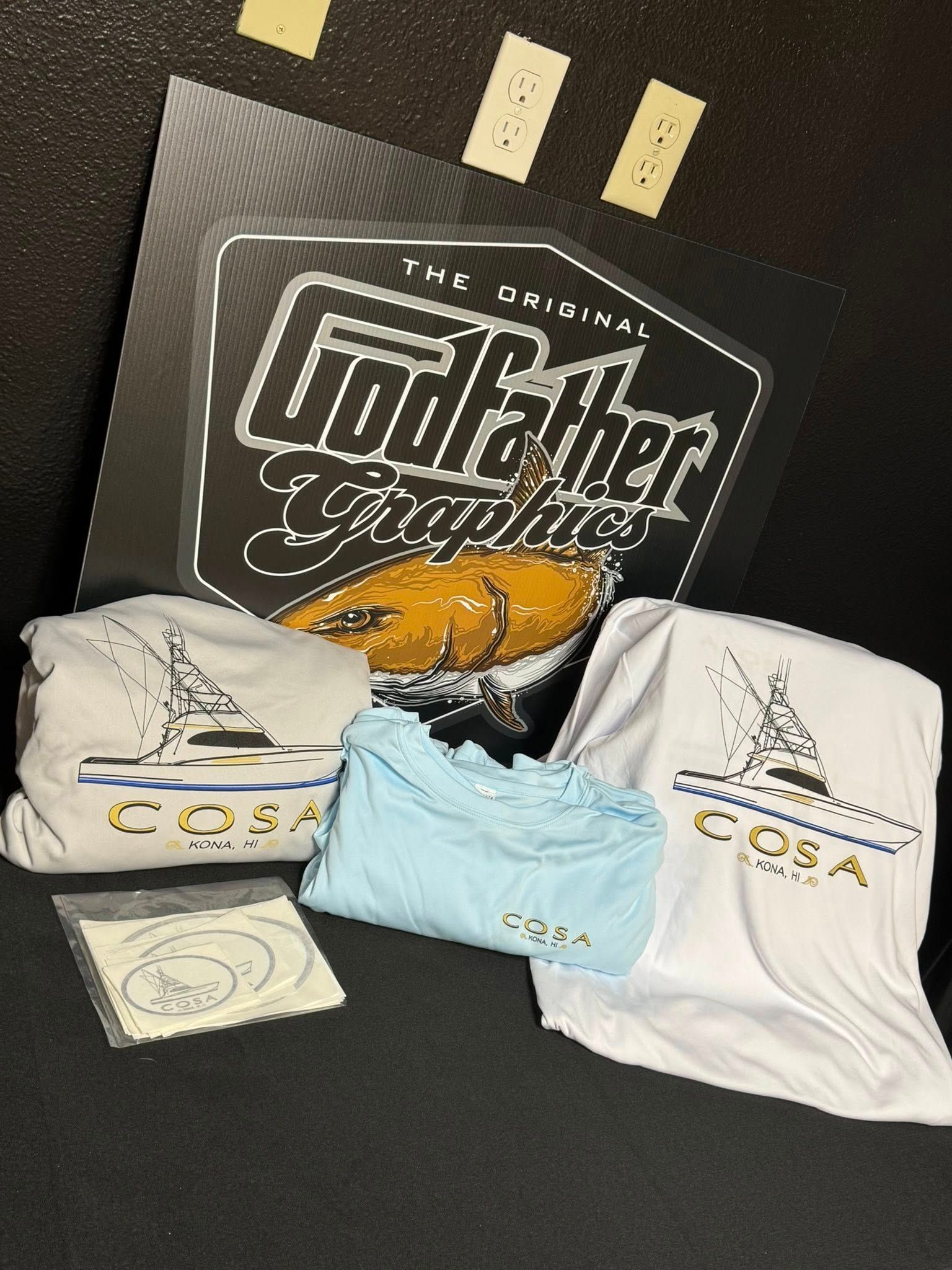 Godfather Graphics merchandise including shirts, a sticker, and a logo, in various colors.