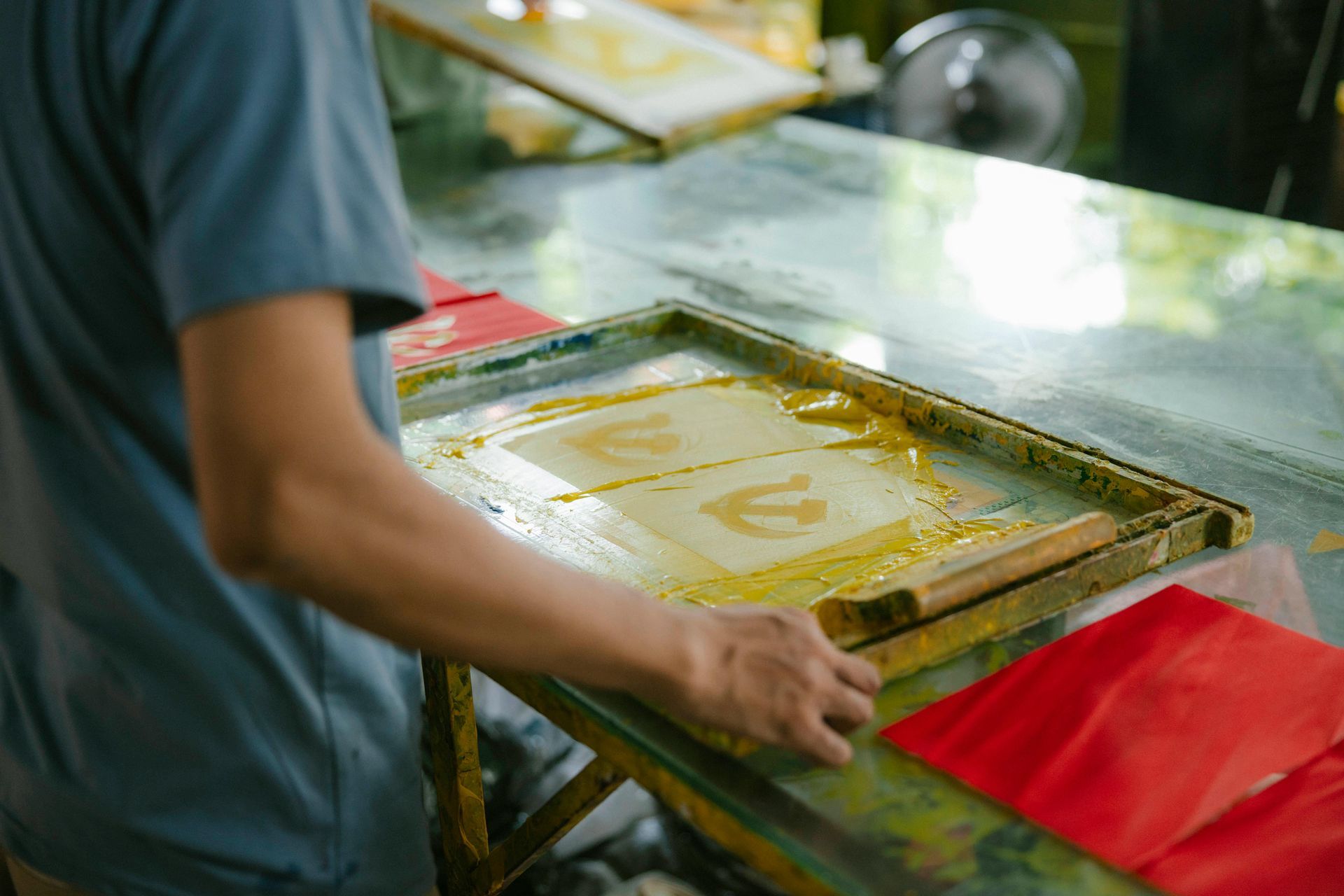 Person using a roller to print on paper with yellow ink. A red paper is nearby.