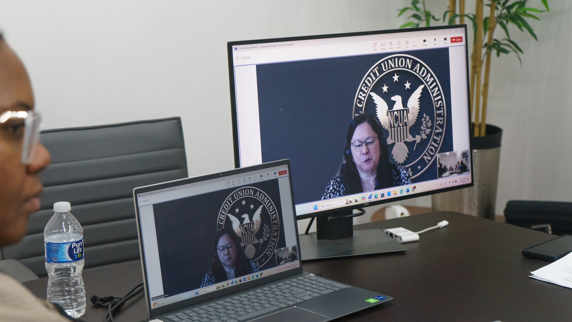 Woman attending a video call, visible on a laptop and monitor, in an office setting.