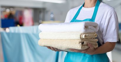 Woman holding a stack of folded white and beige towels in a laundry room.