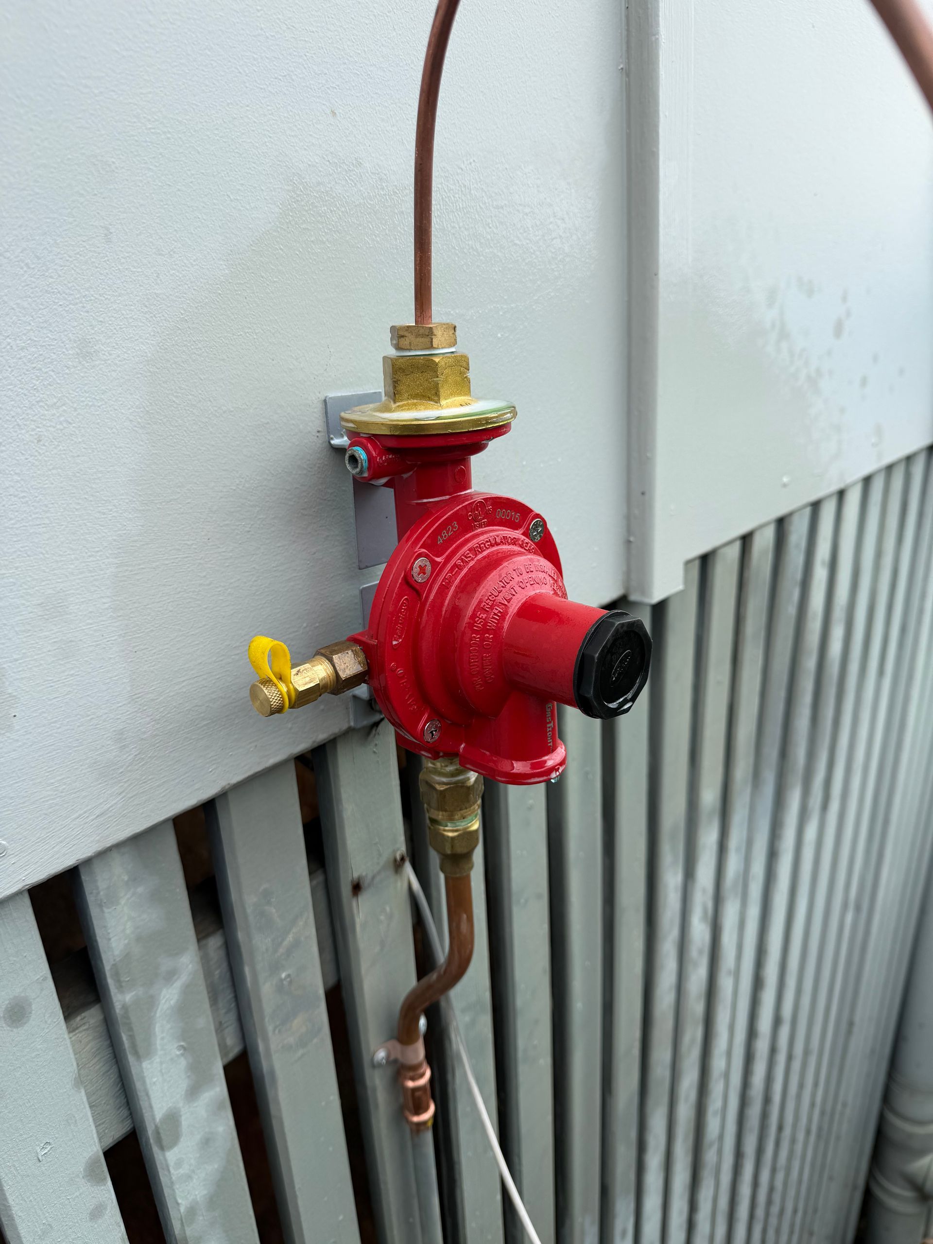 Red industrial gas regulator with brass fittings mounted on a wall, with copper tubing attached.— Truflow Plumbing & Gas Solutions in Rockhampton City, QLD