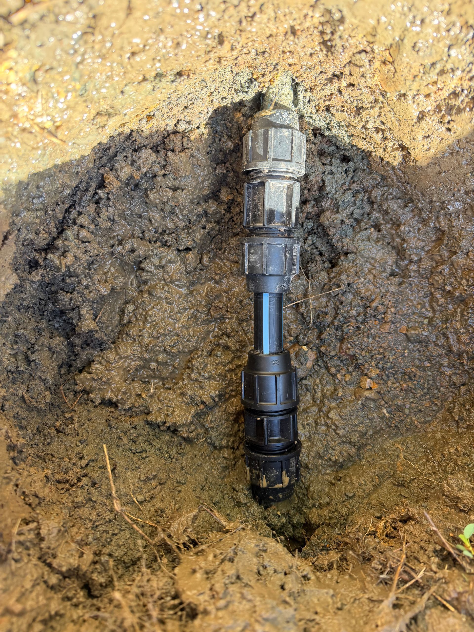 Close-up of a black pipe connector in a dirt hole with exposed soil around it — Truflow Plumbing & Gas Solutions in Rockhampton City, QLD
