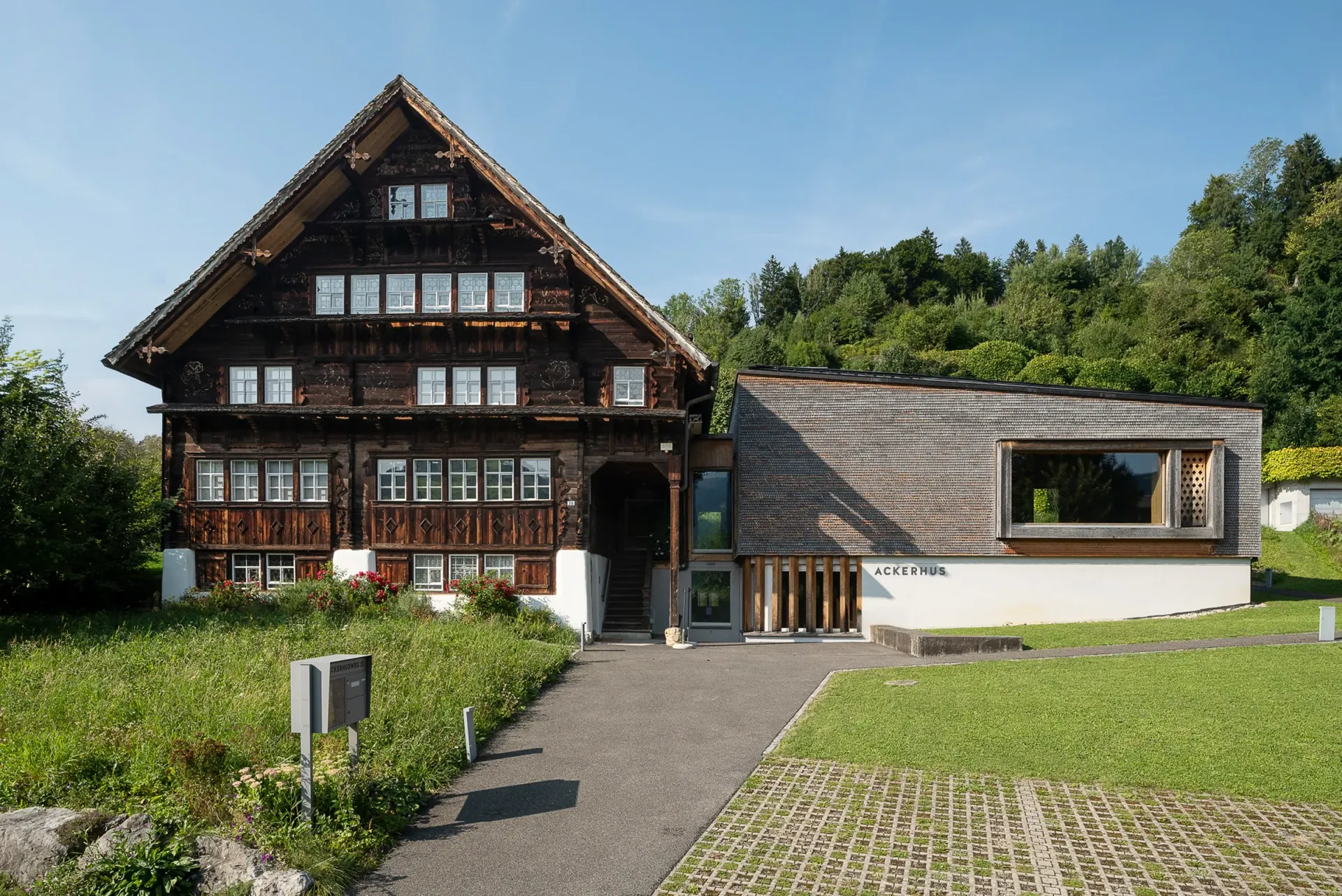 Das Ackerhus  mit modernem Anbau; Rasenfläche, Kiesweg, sonniger Tag.