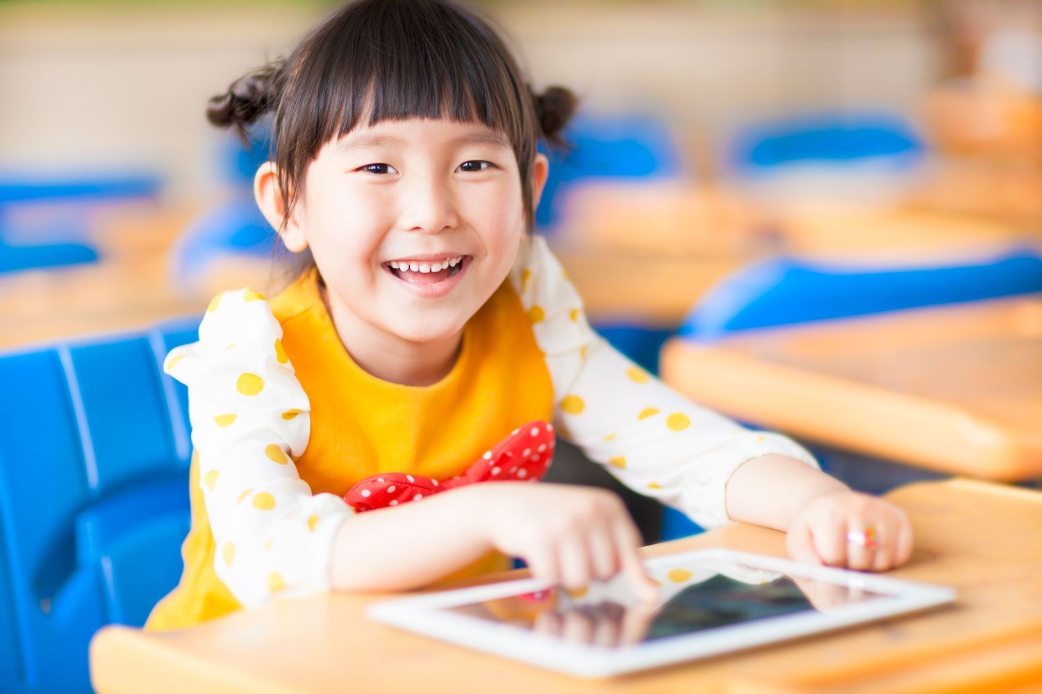 A little girl is smiling while using a tablet